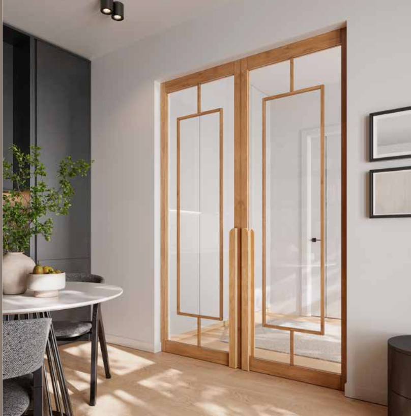 Modern double glass doors with light oak wood frames and geometric metal mullions, set in a bright contemporary interior with a dining table and chairs visible on the left.